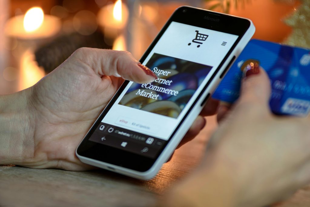 pexels-photo-230544-230544 Woman using smartphone for online shopping with credit card in hand, festive background lighting.